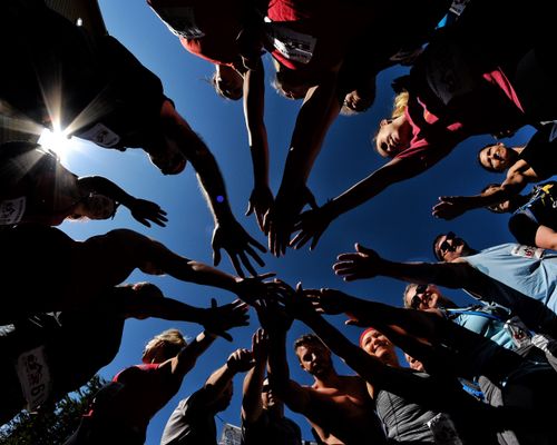 A bottom-up view from the ground toward the sky, as 17 CoreFit members stand in a circle with their hands outstretched toward the center of the image.