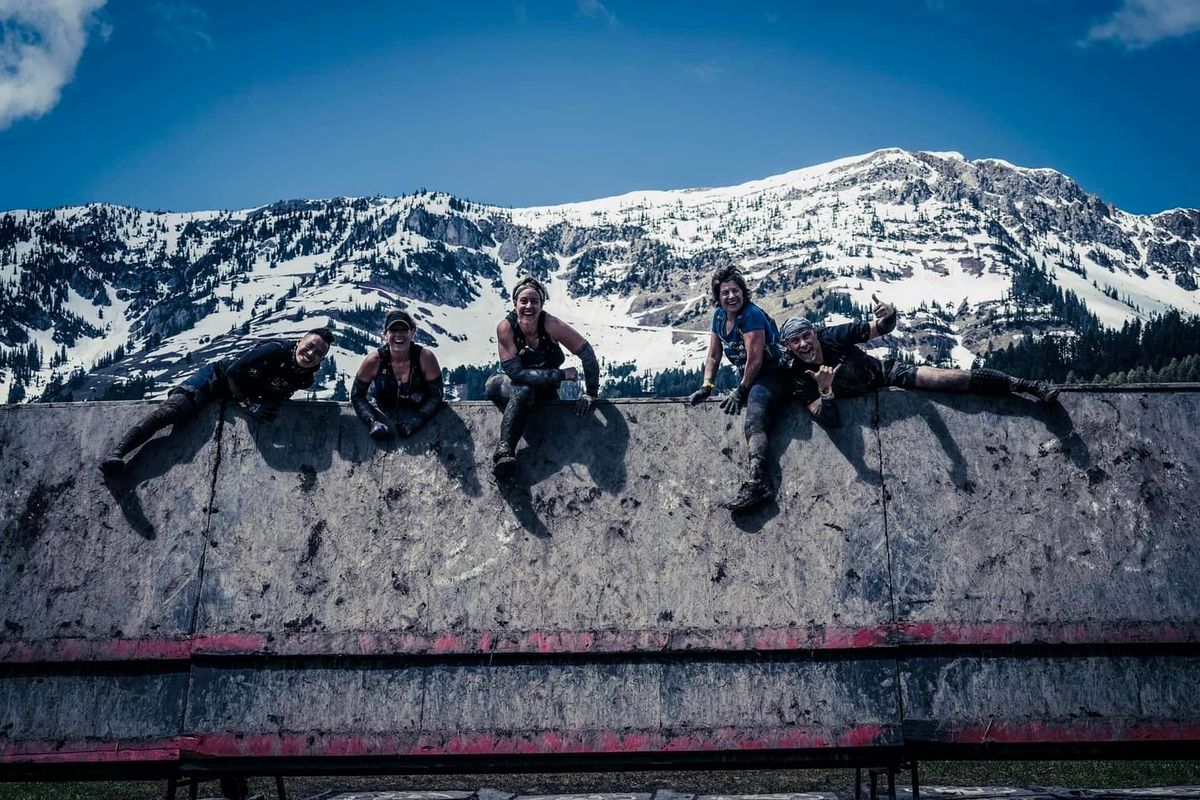 Five CoreFit members pose atop a wall obstacle at a Spartan race.