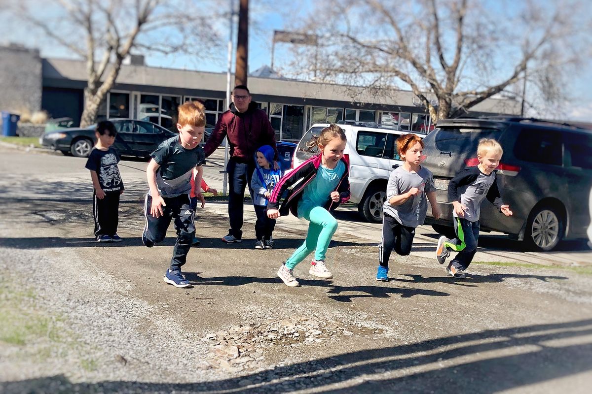 A group of kids, four in front and three behind, running in a relay race down the alley outside the CoreFit building.